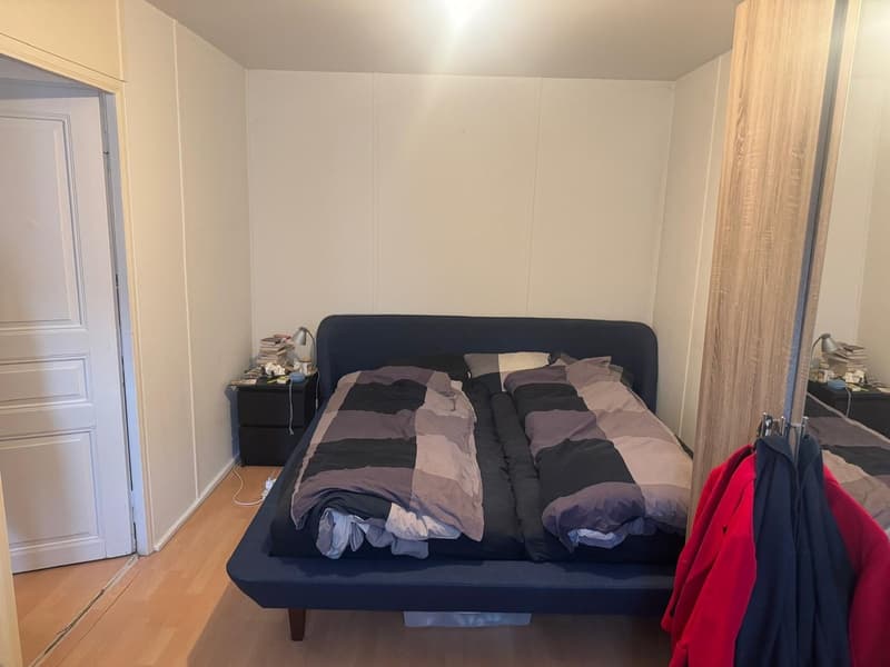 A simple bedroom with a bed, nightstands, and jackets hanging on a hanger.
