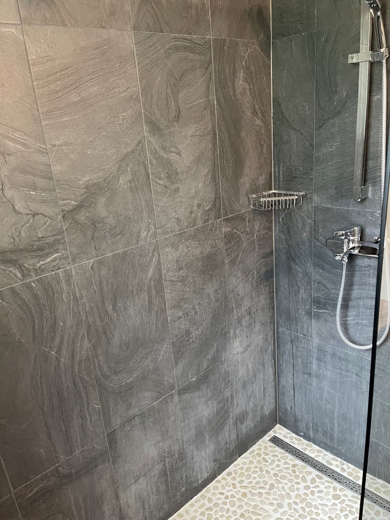 Gray marble tiles, glass shower enclosure, stainless steel shower head, small corner shelf
