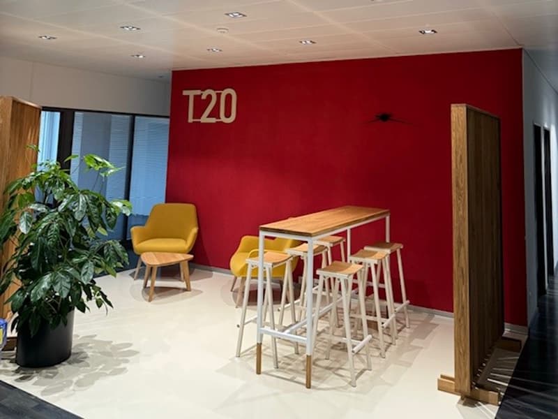 Open office space with red accent wall, wooden furniture including bar stools and chairs, and a potted plant.