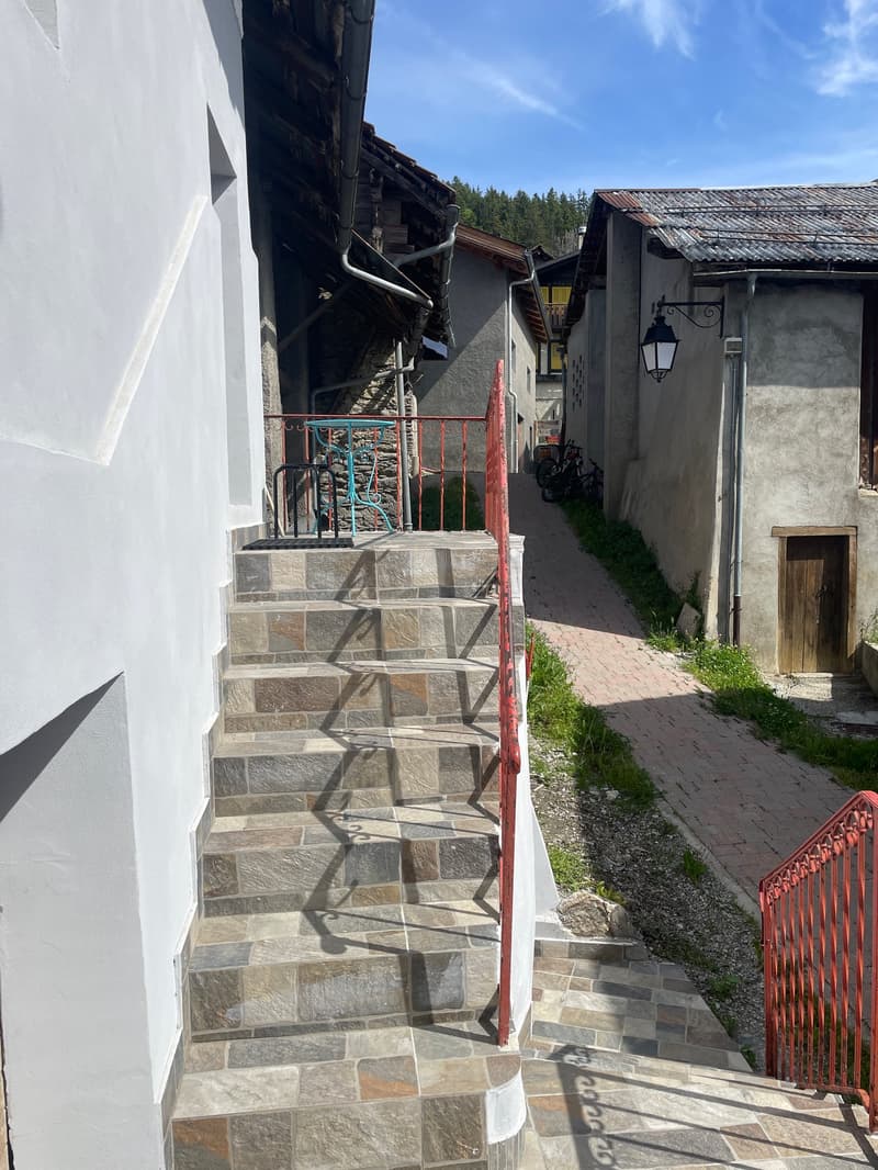 Stone steps leading to the entrance of a building, red railings, bicycles parked on the side, tiled walkway, small trees in the distance