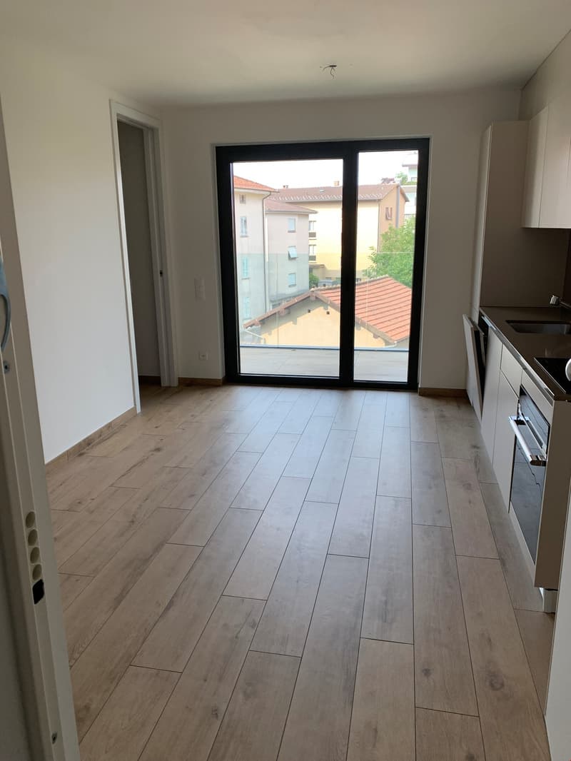 Spacious living room with large windows, hardwood-style tile flooring, and access to a balcony or terrace.