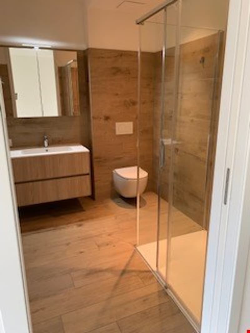 Spacious bathroom with wooden vanity, large mirror, and glass shower enclosure