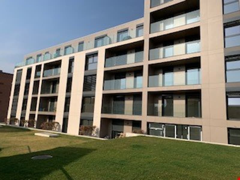 Multi-story apartment building with balconies, glass windows, and a grassy area in the foreground.