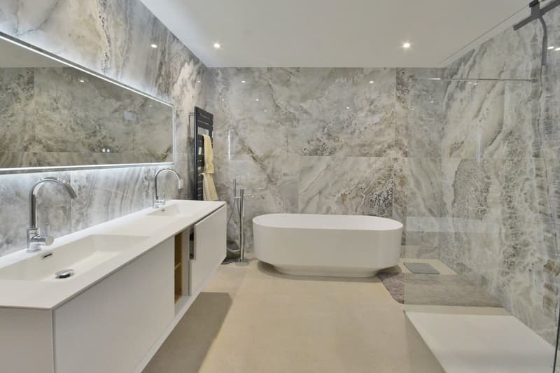 modern bathroom, marble walls, white bathtub, double sink, large mirror, towel rack