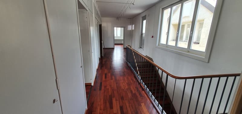 Spacious hallway with hardwood flooring, white walls, and a wooden railing along the second floor balcony overlooking the hallway below.