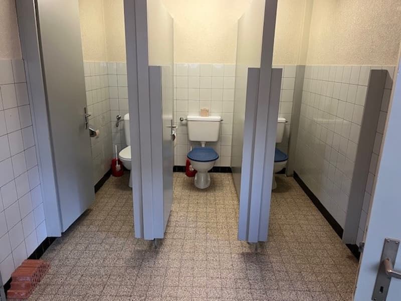 Three cubicles with toilets and white tiled walls