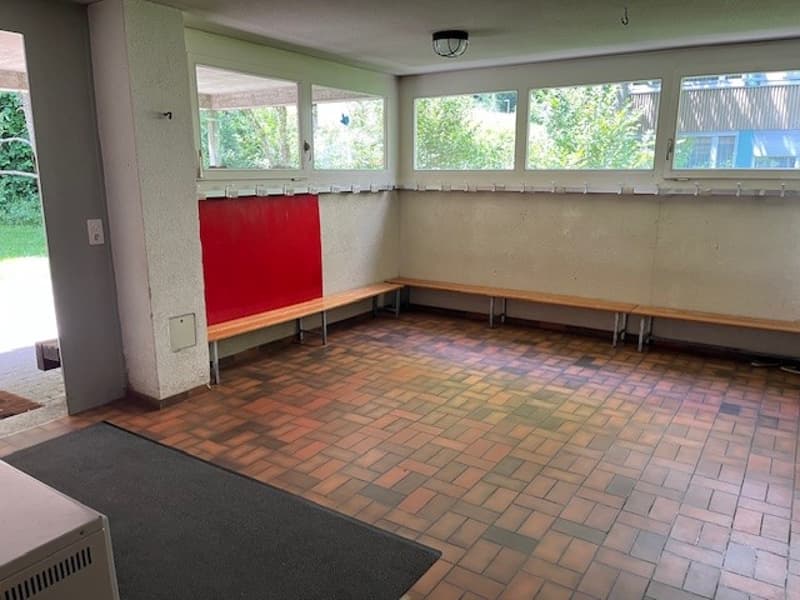 empty room, wooden benches, red wall, brick floor, large windows, lamp