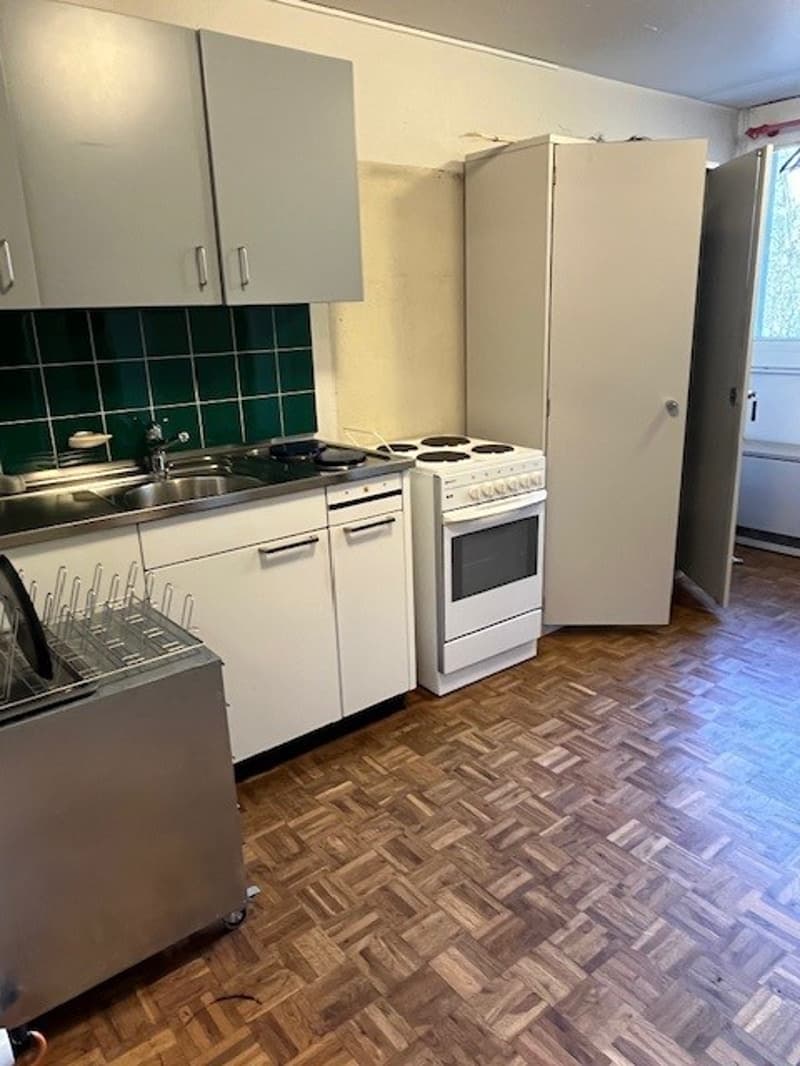 empty kitchen with wooden floor, gas stove, white cabinetry, sink, green tiles, dishwasher