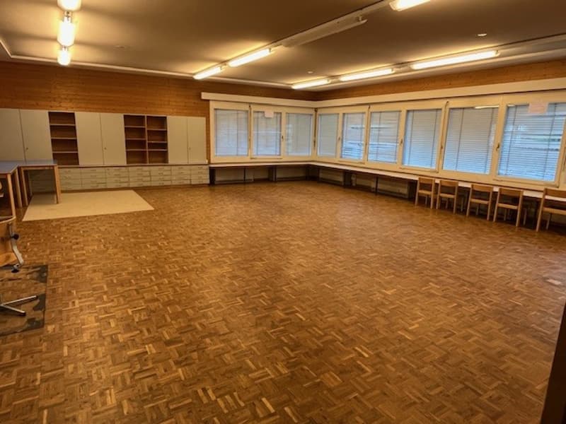 large room, hardwood floors, white cabinets, long wooden bench, windows, tables