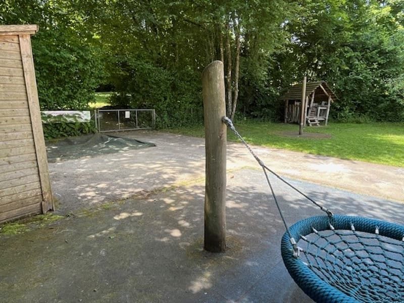 Swing set, paved path, wooden shed, lush trees, wooden gate, small wooden house, grassy field