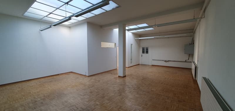 Empty room with wooden floor, white walls, glass windows, and ceiling lights