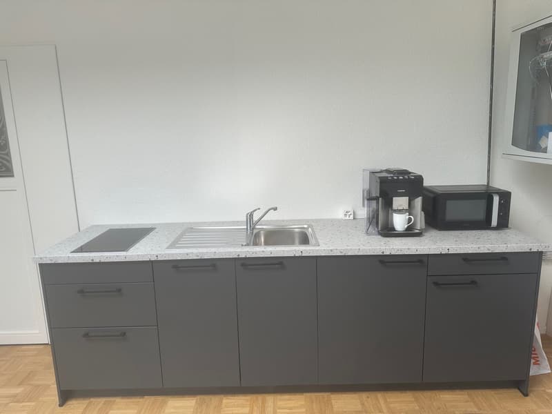 modern kitchen with gray cabinets, granite countertop, stainless steel sink, induction cooktop, coffee machine, microwave, and a white door