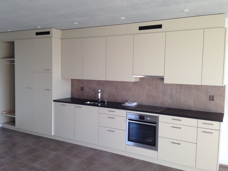 Modern kitchen with white cabinets, black countertops, built-in oven, and tile flooring