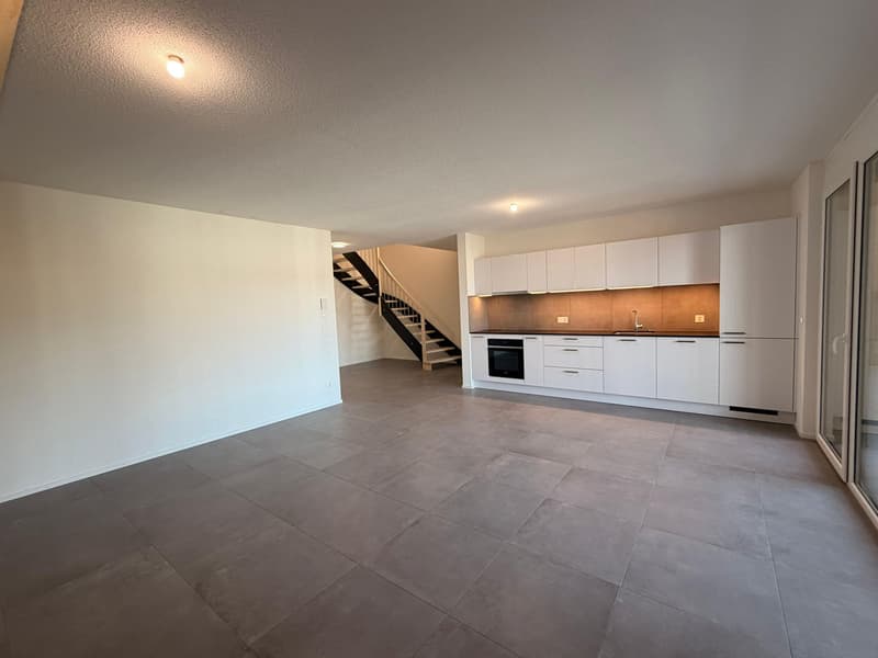 Spacious room with white walls, gray tiles, and white cabinets in the kitchen area