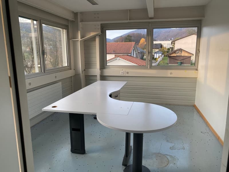 large room with a central desk, windows, white walls, white floor, wall mounted radiators, mounted shelves, power outlets, white ceiling