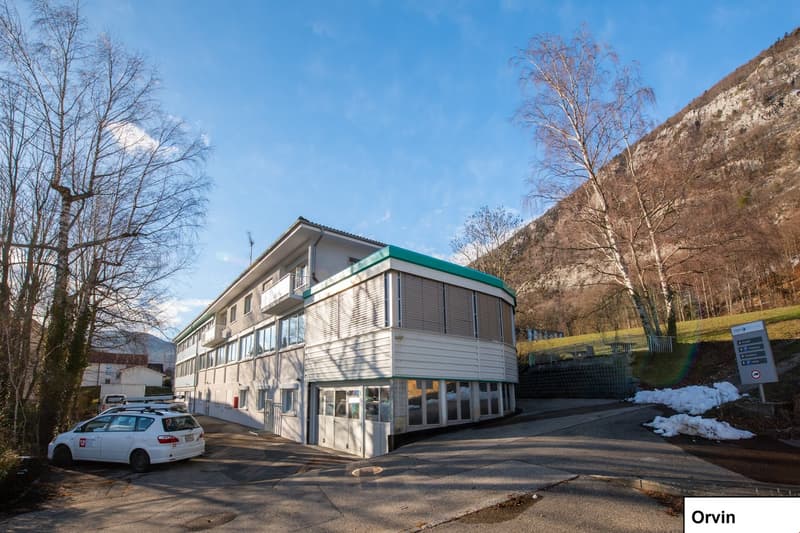 modern multi-story building with glass windows and a slanted roof, located on a street, surrounded by trees and snow