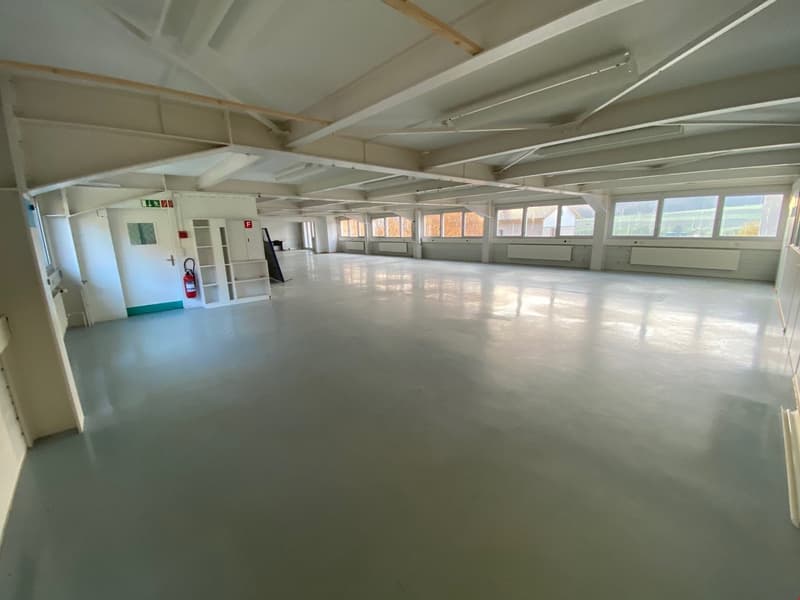 Spacious room, concrete floor, white walls, multiple windows, emergency exit door, fire extinguisher