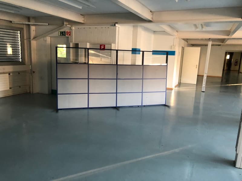 Large open space, gray concrete floor, metal barrier in middle, two doors, high ceilings