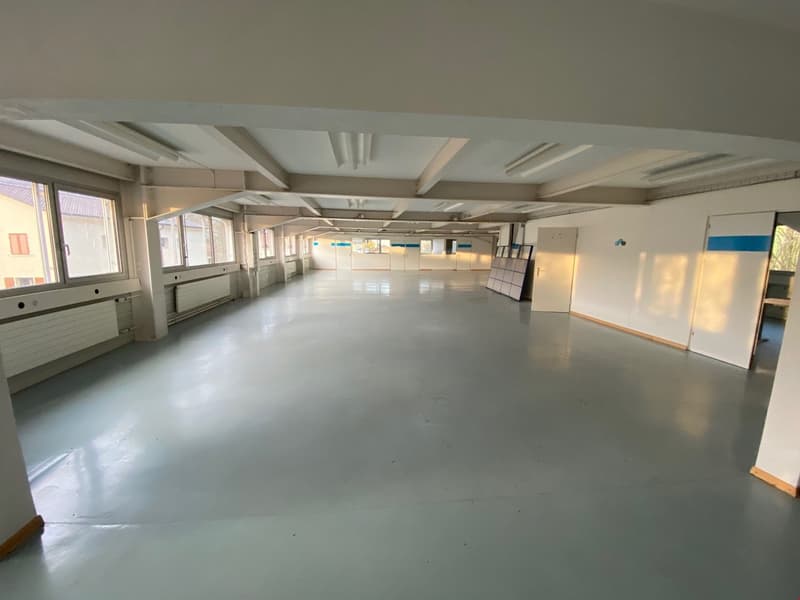 empty room, white walls, concrete floor, radiators, ceiling lights, windows with view of outside building