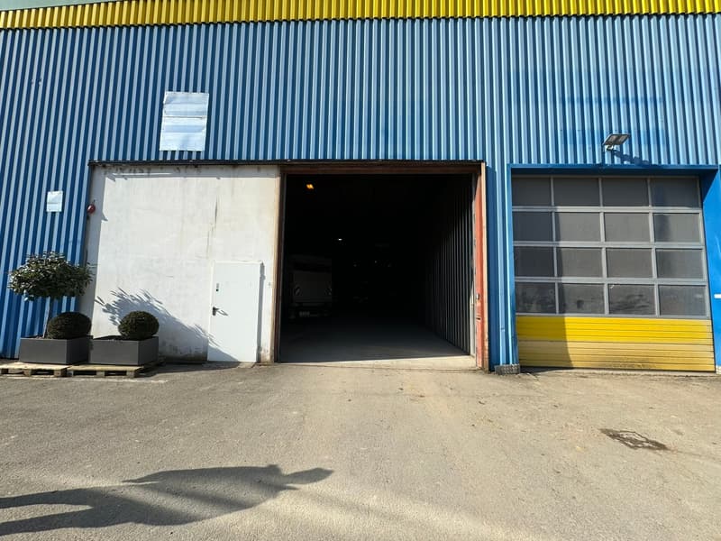 large storage building with double doors open, two entry points, shrubs, paved parking lot