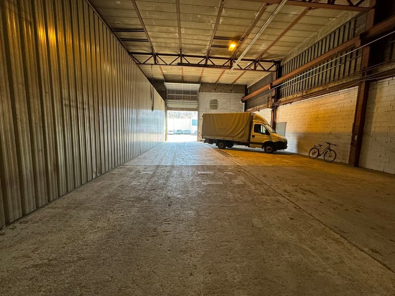 Large industrial building with metal walls, concrete floor, open door, vehicle parked, bicycle leaning on the wall