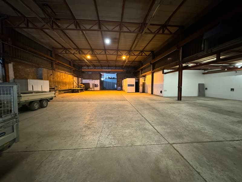 industrial space, high ceiling, steel beams, concrete floor, wide entrance, fenced area, trucks parked