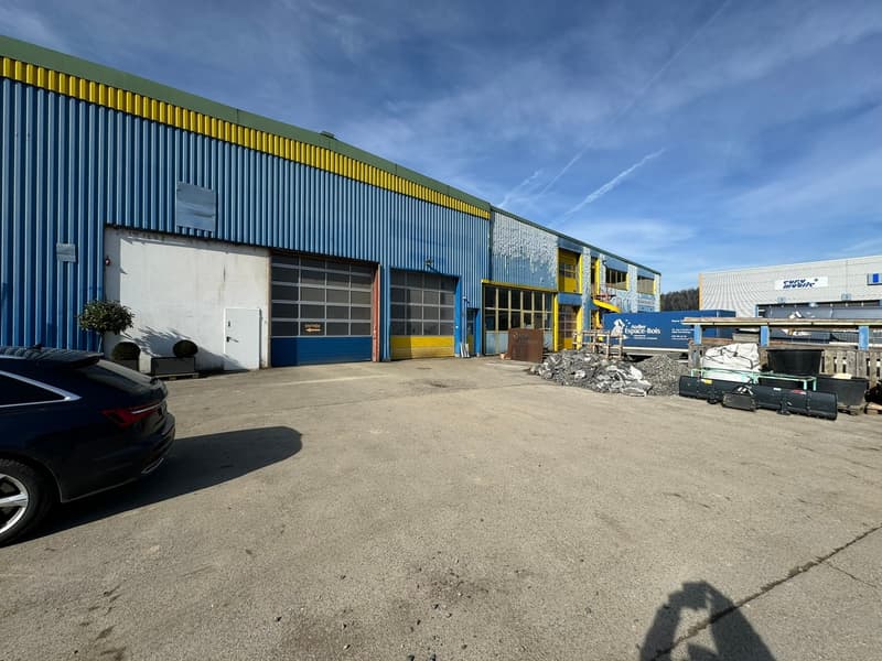 Industrial building with two garage doors, concrete parking lot, and a parked car.