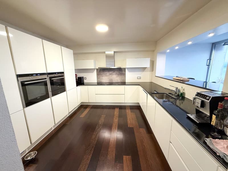 modern kitchen with white cabinets, wooden floor, black countertops, integrated appliances, sink with faucet, kitchen island with coffee machine and wine bottle