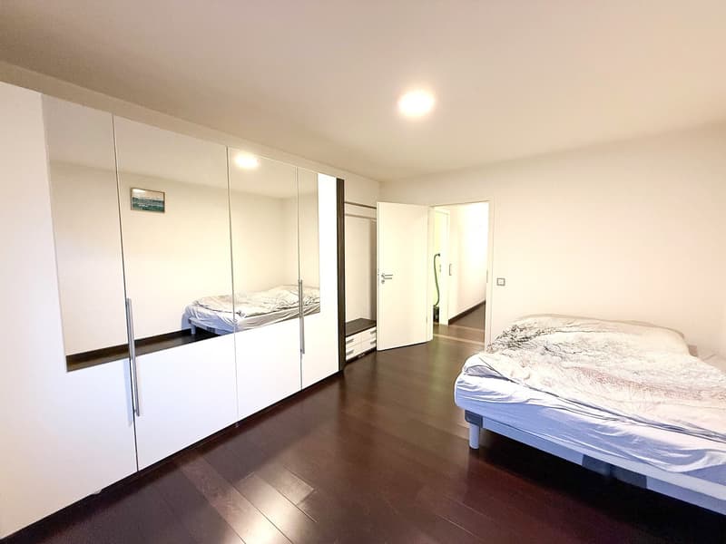 Bedroom with white walls, hardwood floor, two single beds, built-in wardrobe with mirrored doors, and two small drawers