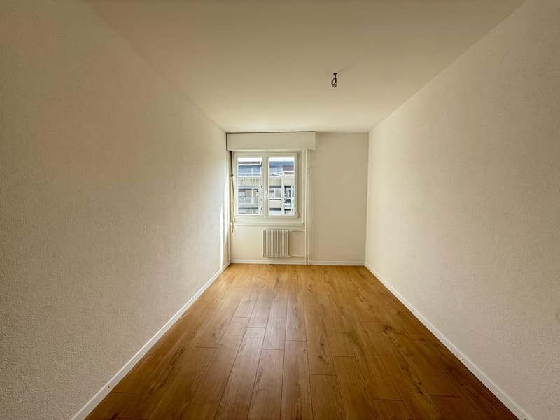 Empty room with wooden floor, white walls, window with white frame, white radiator