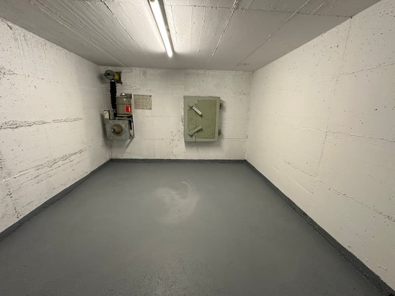 Empty room with white walls, gray floor, and two electrical boxes on the wall