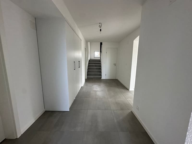 Empty hallway with white walls, gray tiled floor, white built-in wardrobes, staircase, and a door.