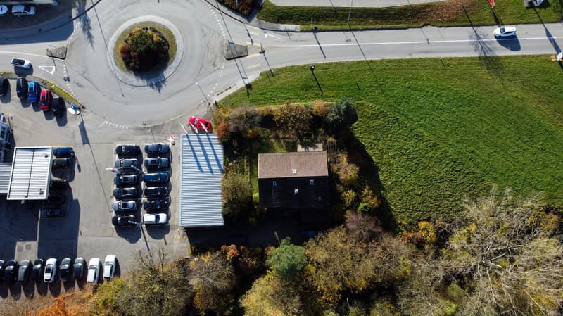 Carpark with multiple cars parked, a single house, and a round roundabout.