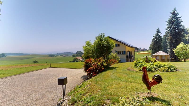 House in the countryside with solar panels on the roof, driveway, well-maintained garden, and distant fields