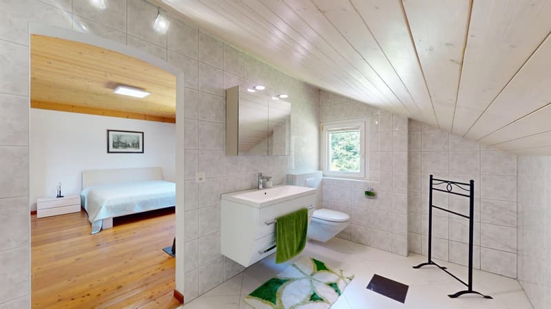 Bathroom with a white toilet, white sink, green towel, wooden floors, white tiles, and a picture frame.