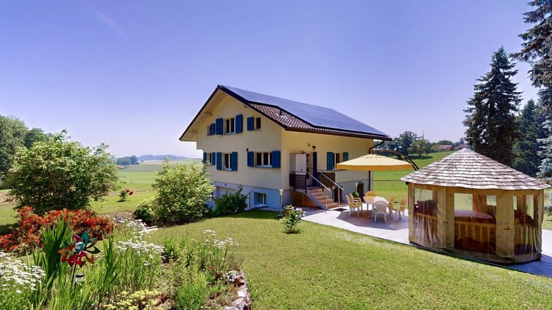 2 story house, yellow exterior, solar panels on the roof, terrace, garden, gazebo, green lawn, dining area with table and chairs, trees