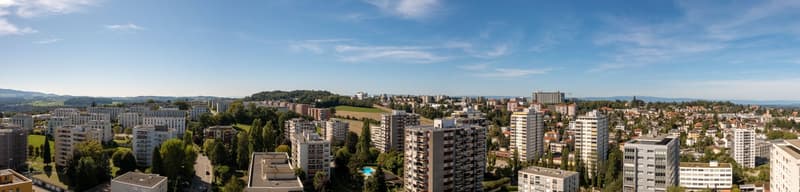 Aerial view of a city with many high-rise buildings and a lush green park in the foreground, mountains in the distance