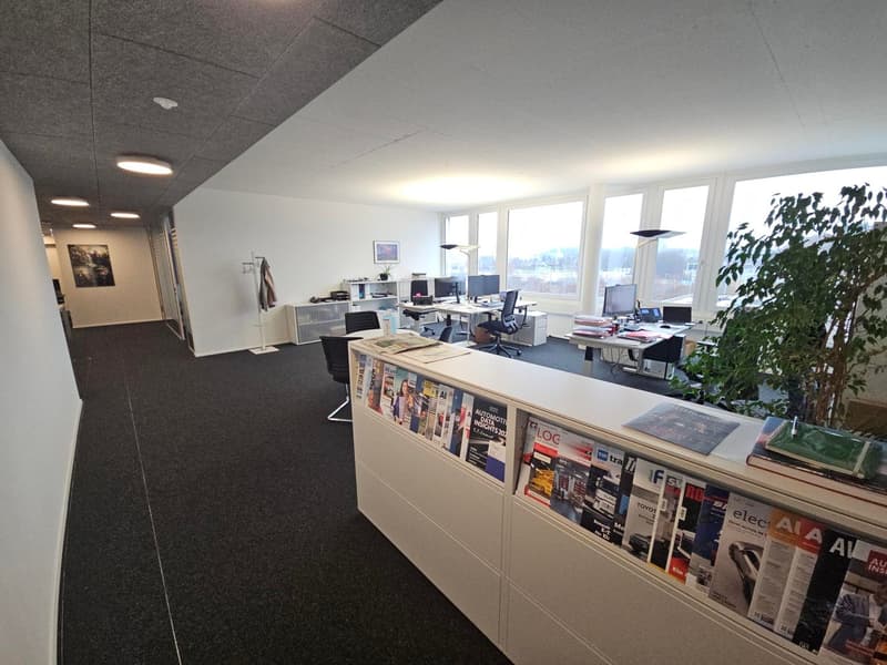 modern office with several desks, computers, large windows, reception desk with magazines