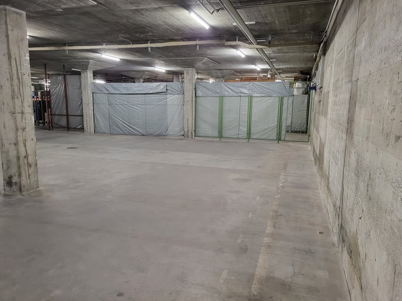 Empty concrete underground parking with white walls, white ceiling, concrete floor, covered with white cloths, metal fence with green poles, metal poles on the floor