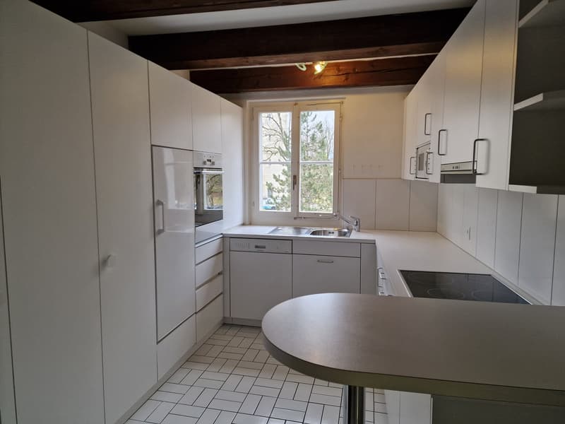 Modern kitchen with white cabinets, stainless steel appliances including a dishwasher, tile flooring, and a large window providing natural light