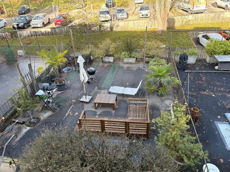 Wooden seating furniture, coffee table, small charcoal grill, potted plants, tables, chairs, open area, fenced perimeter, asphalt, parked cars