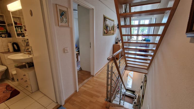 wooden staircase with metal handrail, white walls, ceramic tiles, picture frames on wall, bathroom sink, toilet, decorative items