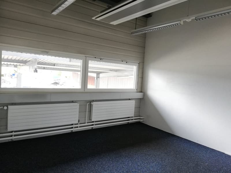 Empty room with white walls, metal radiators, ceiling lights, and a large window overlooking outside.