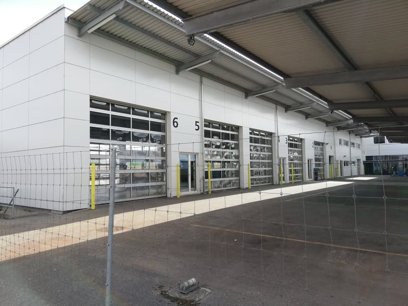 industrial warehouse, multiple large garage doors, fenced parking lot, multiple white panels on the wall