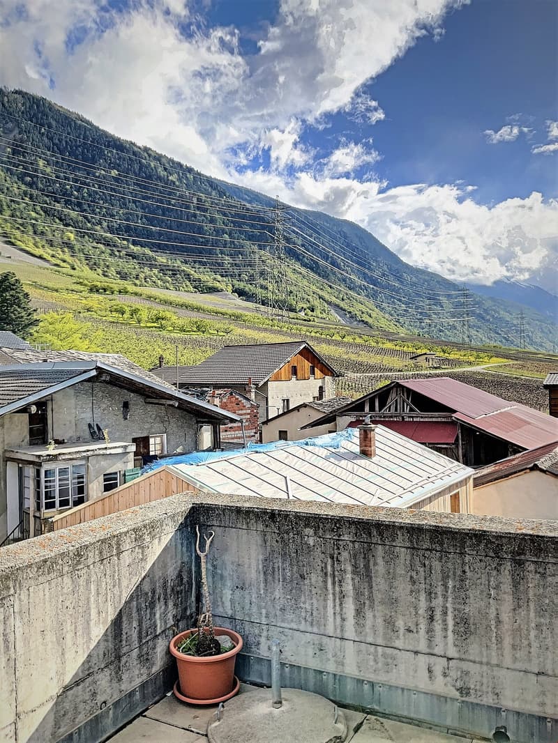 Stone walled terrace with concrete railing overlooking a small village, mountains, fields