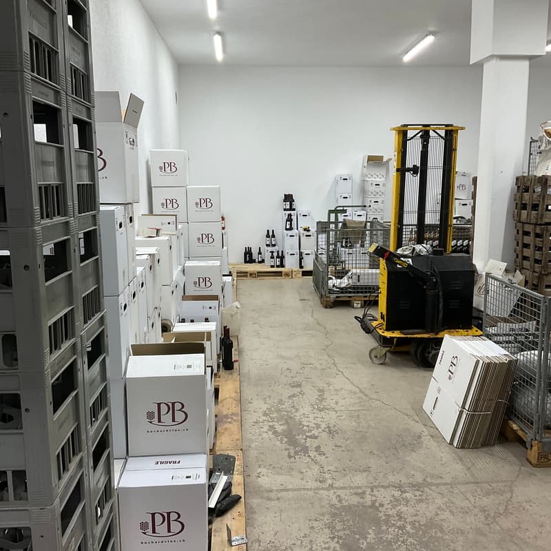Storage warehouse with boxes of wine, racks, a forklift, and pallets.