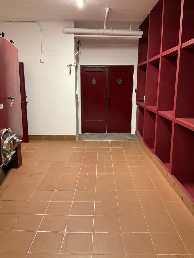 Empty room, red tiled floor, red shelves, two double doors, metal pipe on the wall