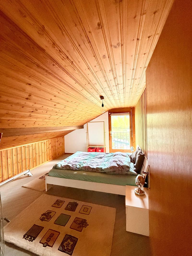 Bedroom with slanted ceiling, double bed, nightstand, carpet, window with balcony