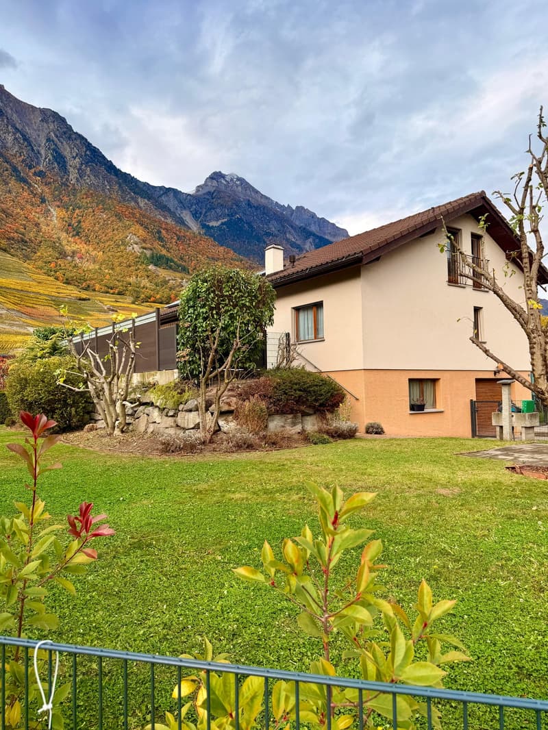 2 story house, beige exterior, mountains in the background, lush garden