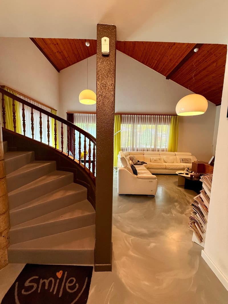stairs, wooden railing, white couch, center column, lamp, white flooring